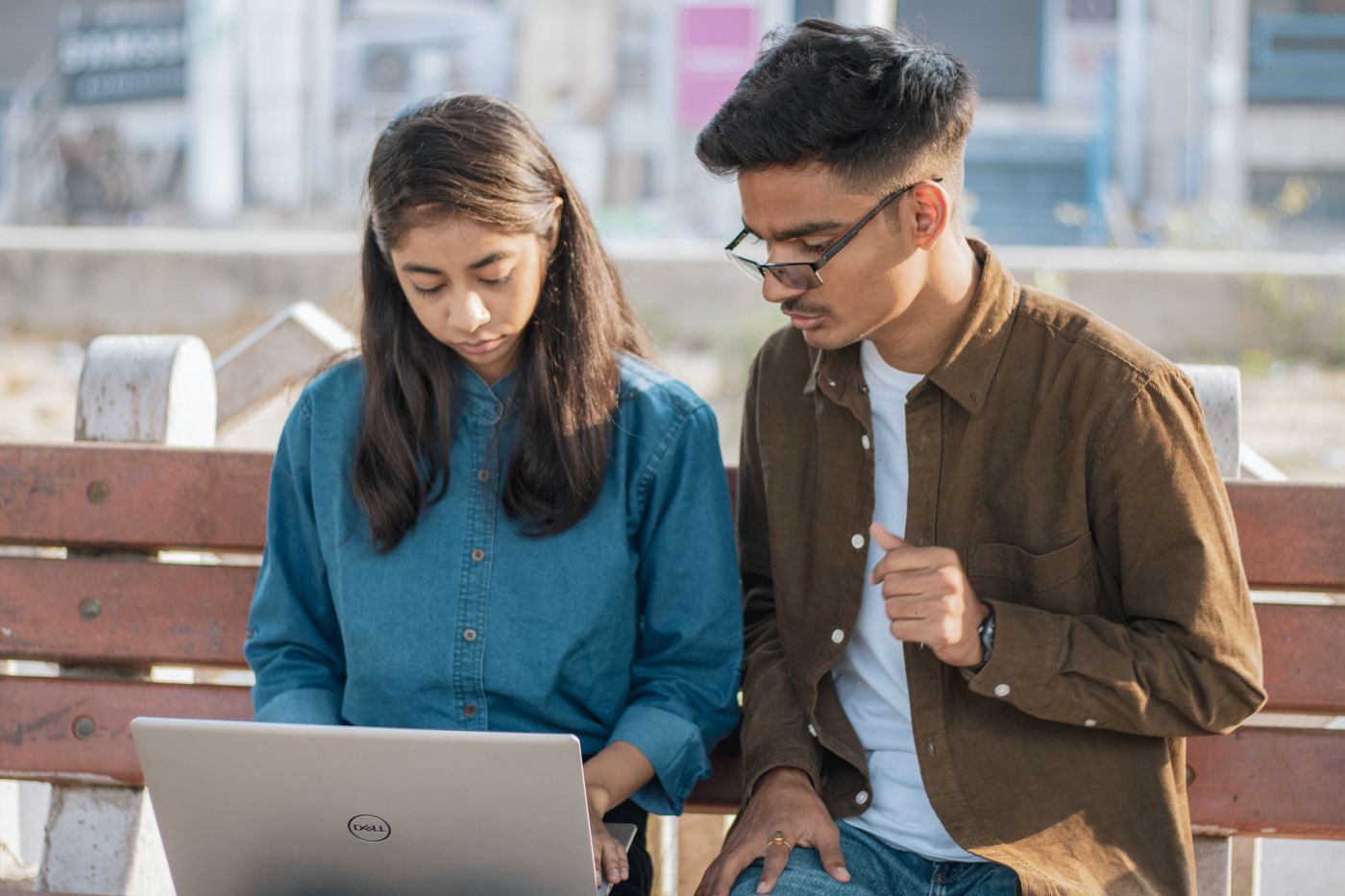 Two young Indian adults studying together on a laptop in a modern urban setting
